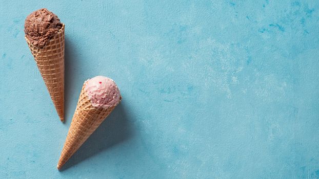 Various ice cream scoops in cones with copy space. Colorful ice cream in cones chocolate, strawberry, blueberry, pistachio or matcha, biscuits chocolate sandwich cookies on blue background. Top view