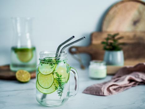 Cold drink in mason jar with metal straws on kitchen table. Lemonade or detox water with lime and thyme in glass jar wit metal straw indoor. Recyclable straws, zero waste concept