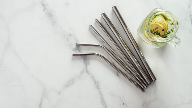 Metal drinking straws and cold drink in glass mason jar on white marble background. Top view or flat lay. Copy space for text or design. Recyclable straws, zero waste concept. Banner.