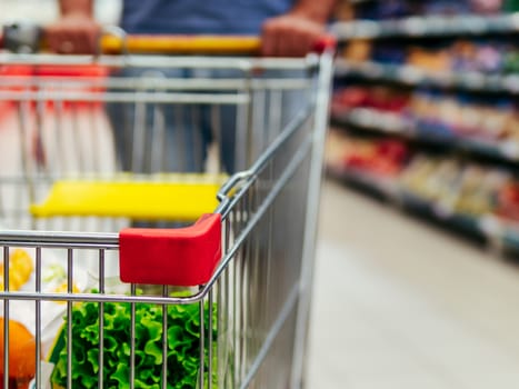 Shopping cart in supermarket. Caucasian or latin man hands hold shopping trolley in supermarket aisle.