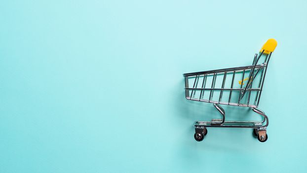 Shopping cart on blue background. Top view or flat lay. Shop trolley at supermarket as sale, discount, shopaholism concept with copy space for text or design. Consumer society trend.