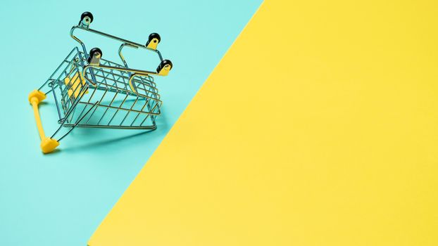 Empty inverted shopping cart on blue and yellow background. Inverted toy trolley on bright colorful background, copy space for text or design.