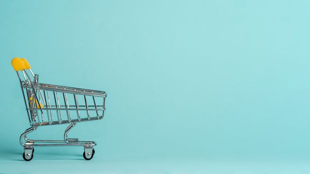 Shopping cart on blue background. Shop trolley at supermarket as sale, discount, shopaholism concept with copy space for text or design.