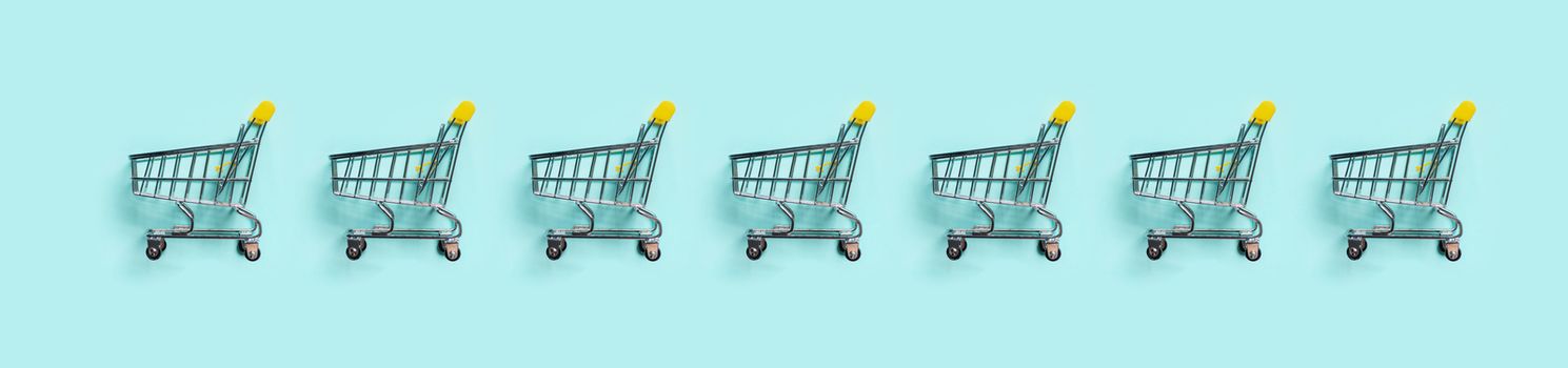 Shopping cart in row on blue background. Minimalism style. Toy trolley for supermarket. Top view or flat lay. Sale, discount, shopaholism concept. Consumer society trend.
