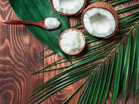 Top view of coconut MCT oil in bowl and in spoon and halved coco-nut on wooden table. Health Benefits of MCT Oil. MCT or medium-chain triglycerides, form of saturated fatty acid. Flat lay. Copy space