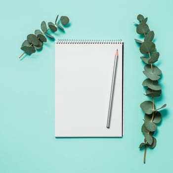 Blank notebook, pencil and eucalyptus on blue background. Empty notebook paper and eucalyptus branch on pastel blue background with copy space for text or design. Flat lay, top view, copyspace, square