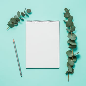 Blank notebook, pencil and eucalyptus on blue background. Empty notebook paper and eucalyptus branch on pastel blue background with copy space for text or design. Flat lay, top view, copyspace, square