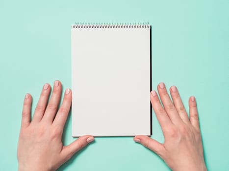 Blank paper notebook and female hands. Empty paper sketchbook and woman hands on blue background. Top view or flat lay. Copy space for text or design.
