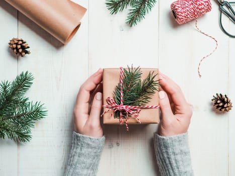 Christmas gift wrapping background.Female hands holding christmas present box wrapped in kraft, top view. Winter holidays concept, flat lay.Woman with pink pastel matte manicure packing Christmas gift