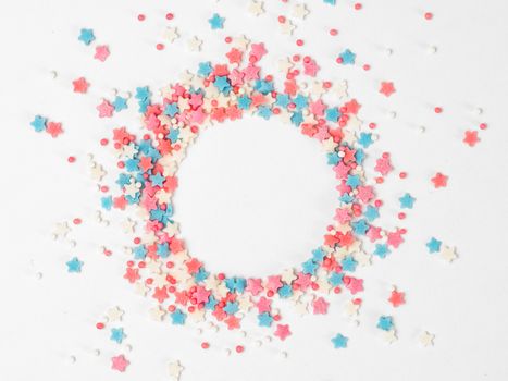 Festive border frame of colorful pastel sprinkles on white background with copy space in center. Sugar sprinkle dots and stars in round shape, decoration for cake and bakery. Top view or flat lay