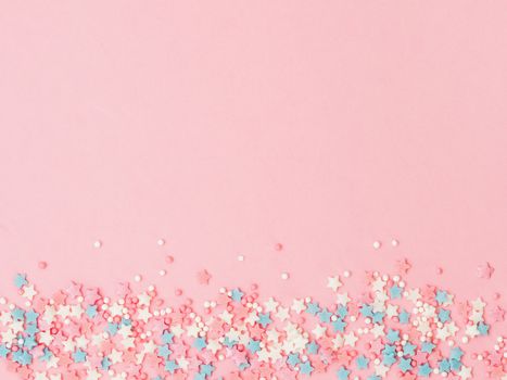 Festive border frame of colorful pastel sprinkles on pink background, copy space top. Sugar sprinkle dots and stars, decoration for cake and bakery. Top view or flat lay