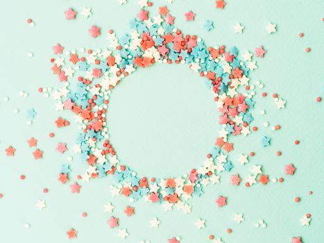 Festive border frame of colorful pastel sprinkles on blue background with copy space in center. Sugar sprinkle dots and stars in round shape, decoration for cake and bakery. Top view or flat lay