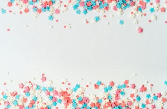 Festive border frame of colorful pastel sprinkles on white background with copy space in center. Sugar sprinkle dots and stars, decoration for cake and bakery. Top view or flat lay. Banner