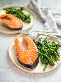 Ready-to-eat grilled salmon steak and greens - baby broccoli or broccolini and spinach on rustic craft plate over gray background. Keto diet dish. Vertical