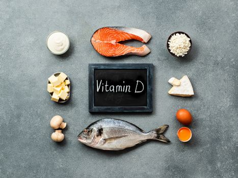 Vaitamin D sources concept. Fish, salmon, dairy products, eggs, mushrooms and chalkboard with Vitamin D words on gray stone background. Top view or flat lay.