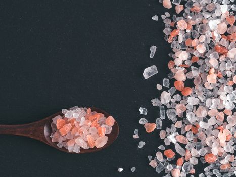 Himalayan pink salt in spoon on black stone background. Copy space