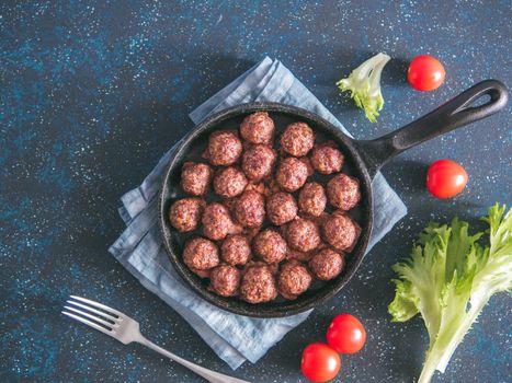 Homemade roasted beef meatballs in cast-iron skillet on dark blue background. Top view or flat-lay. Copy space for text.