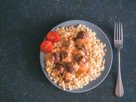 Bulgur dish idea and recipe. Bulgur with homemade roasted beef meatballs on dark blue background. Copy space for text. Top view or flat-lay.