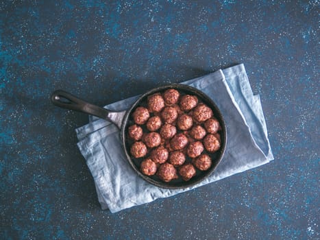 Homemade roasted beef meatballs in cast-iron skillet on dark blue background. Top view or flat-lay. Copy space for text.