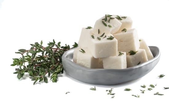 Diced soft cheese in rustic plate and fresh thyme isolated on white background with clipping path.