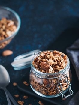 Homemade granola in glass jar on dark table. Ingredients for healthy breakfast. Copy space for text. Low key. Selective focus. Shallow DOF