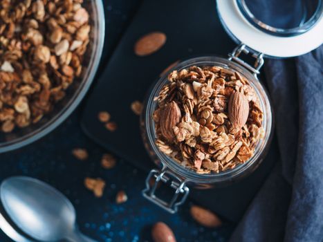 Homemade granola in glass jar on dark table. Ingredients for healthy breakfast. Copy space for text. Low key. Selective focus. Shallow DOF. Top view or flat-lay.
