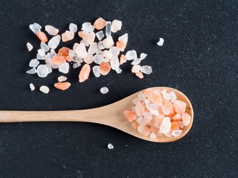 Himalayan pink salt in spoon on black stone background. Copy space