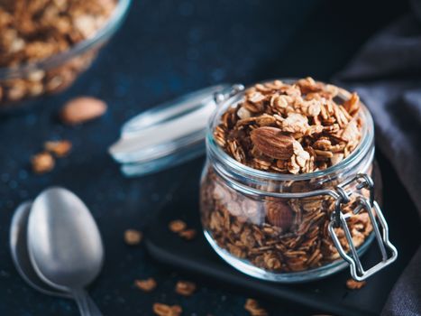 Homemade granola in glass jar on dark table. Ingredients for healthy breakfast. Copy space for text. Low key. Selective focus. Shallow DOF