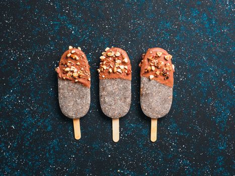 Chia popsicle with chocolate and nuts on blue background. Healthy recipe and idea homemade vegan popsicle ice cream. Easter dessert idea. Copy space for text. Top view or flat-lay.