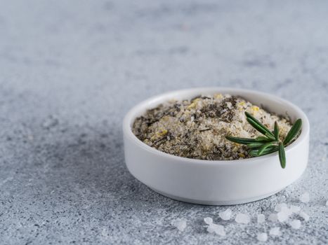 Sea salt scented herb rosemary and lemon zest. Sea salt with aromatic herbin small bowl on gray cement background. Scented salt and ingerdients. Copy space