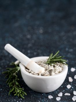 Close up view of mortar and pestle with sea salt scented rosemary and lemon zest. Sea salt scented herb rosemary on dark blue background. Scented salt and ingerdients. Copy space