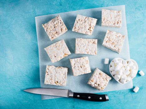 Homemade square bars of Marshmallow and crispy rice and ingredients on blue background. American dessert with marshmallow and crispy rice. Top view. Copy space