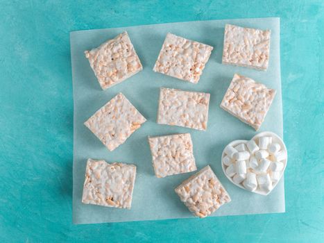 Homemade square bars of Marshmallow and crispy rice and ingredients on azure blue background. American dessert with marshmallow and crispy rice. Top view. Copy space