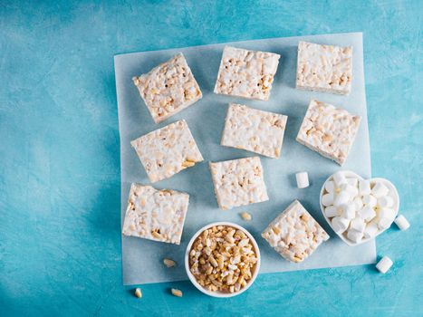 Homemade square bars of Marshmallow and crispy rice and ingredients on blue background. American dessert with marshmallow and crispy rice. Top view. Copy space