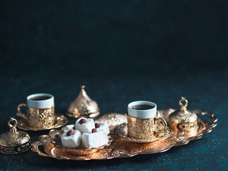 Turkish coffee with delight and traditional copper serving set on dark background. Assorted traditional turkish dilight or lokum and turkish coffee in metal traditional cups.Copy space.Selective focus
