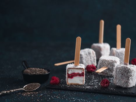 Homemade raw lamington ice cream pops on dark background. Australian sweet dessert lamington with chia and raspberries jam, chocolate and cocoa coat. Vegan food recipe and idea. Copy space for text