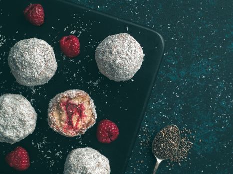 Raw vegan lamington bliss balls with raspberries chia jam on dark background. No baked healthy vegan sweet dessert idea and recipe. Copy space for text. Top view or flat-lay.