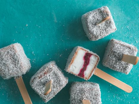 Homemade raw lamington ice cream pops on blue background. Australian sweet dessert lamington with chia and raspberries jam, chocolate and cocoa coat. Vegan food recipe and idea. Top view or flat-lay.