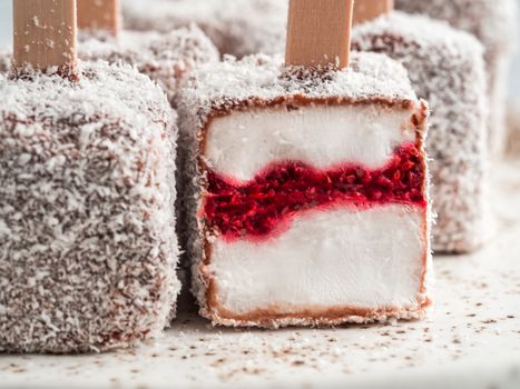 Homemade raw lamington ice cream pops on light background. Australian sweet dessert lamington with chia and raspberries jam, chocolate and cocoa coat. Vegan food recipe and idea. Copy space. Close up