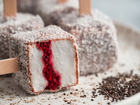 Homemade raw lamington ice cream pops on light background. Australian sweet dessert lamington with chia and raspberries jam, chocolate and cocoa coat. Vegan food recipe and idea. Copy space. Close up