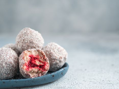Raw vegan lamington bliss balls with raspberries chia jam on gray background. No baked healthy vegan sweet dessert idea and recipe. Top view or flat-lay.