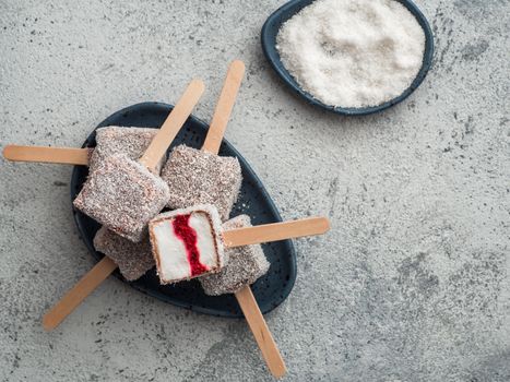 Homemade raw lamington ice cream pops on gray background. Australian sweet dessert lamington with chia and raspberries jam, chocolate and cocoa coat. Vegan food recipe and idea. Copy space. Top view