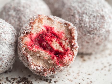 Raw vegan lamington bliss balls with raspberries chia jam on gray background. No baked healthy vegan sweet dessert idea and recipe. Close up