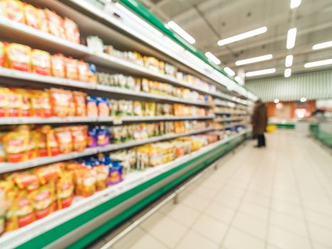 Defocused blur of supermarket shelves with dairy and mayonnaise products in refrigerator. Blur background with bokeh. Defocused image