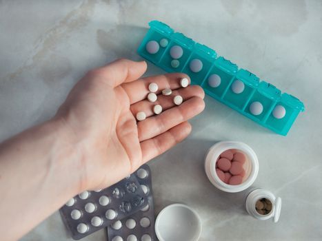 Hand with pills and pillbox. Top view of seven day pill box with pills. Green pill-box over light marble table. Open pill box and open boxes with pills or vitamins. Copy space. Top view or flat-lay.