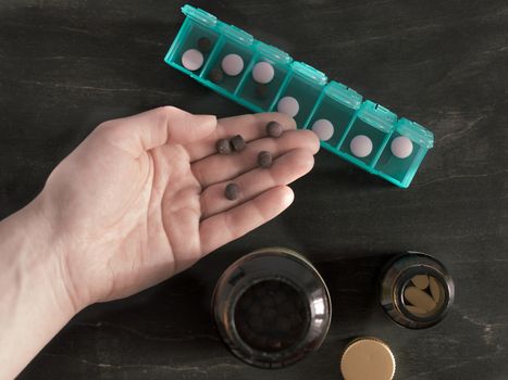 Hand with pills and pillbox. Top view of seven day pill box with pills. Green pill-box over dark wooden table. Open pill box and open boxes with pills or vitamins. Copy space. Top view or flat-lay.