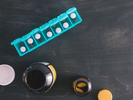 Top view of seven day pill box with pills. Green pill-box over dark wooden table. Open pill box and open boxes with pills or vitamins. Copy space. Top view or flat-lay.