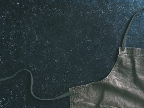 Cooking and kitchen background - trendy denim cotton apron on dark background with copy space. Gray kitchen apron on dark table as kitchen background with space for text. Top view or flat-lay.