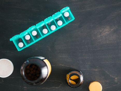 Top view of seven day pill box with pills. Green pill-box with pills visible. Open pill box and jars on dark wooden table. Copy space. Top view or flat lay.Healthy lifestyle and medical concept