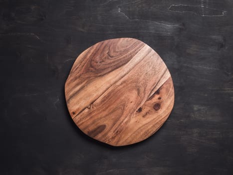 Round wooden tray or cutting board on black table. Top view of empty kitchen trendy rustic wooden tray saw cut imitation on black wooden background. Copy space for text. Food and menu background.